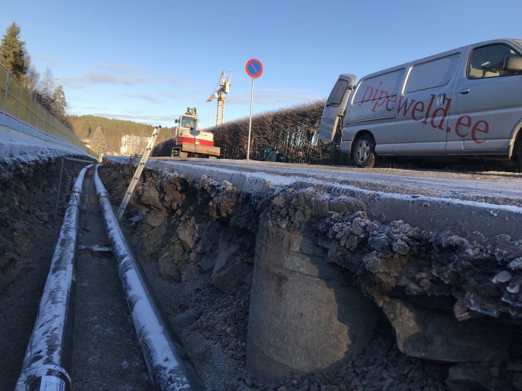 Fjernvarmerør sveiset med gassveising i grøft i Oslo, med firmakjøretøy og logo synlig over grøften.