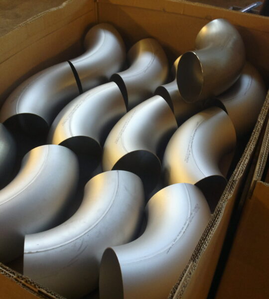 Box of stainless steel pipe elbows prepared for industrial installation by a piping installation company