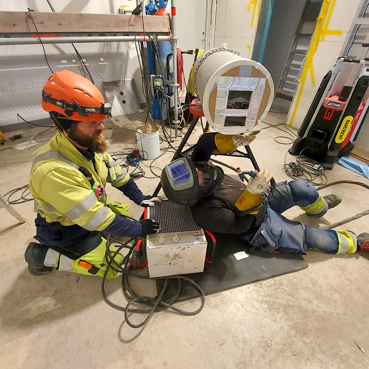 Två montörer under rörinstallationer – en svetsar medan den andra assisterar i en svår position.