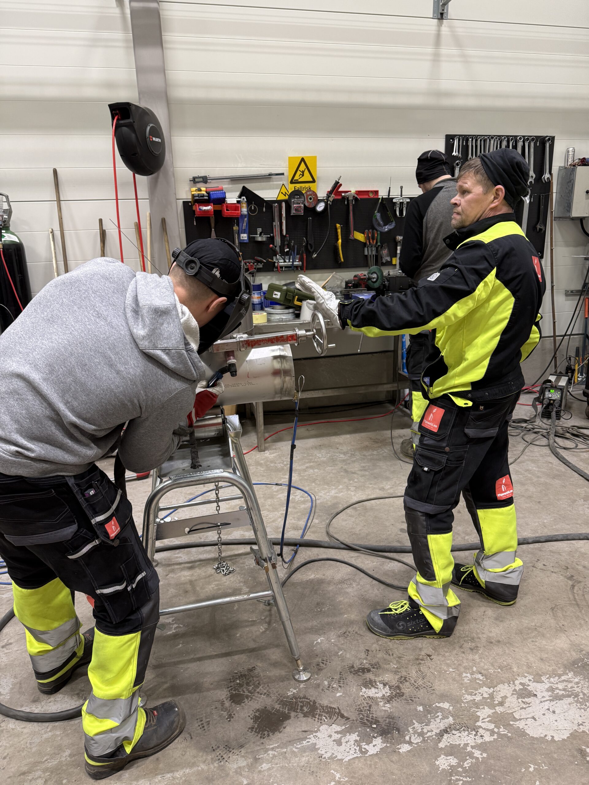 Multi-skilled pipe welder and fitter working in workshop performing TIG welding on stainless steel pipe